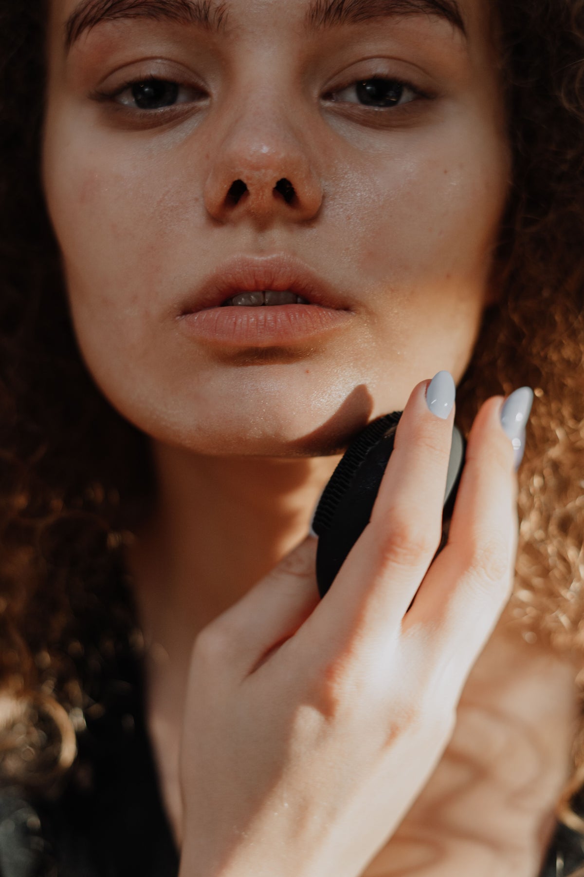 Close portrait of a woman with curly hair, hand resting on her cheek