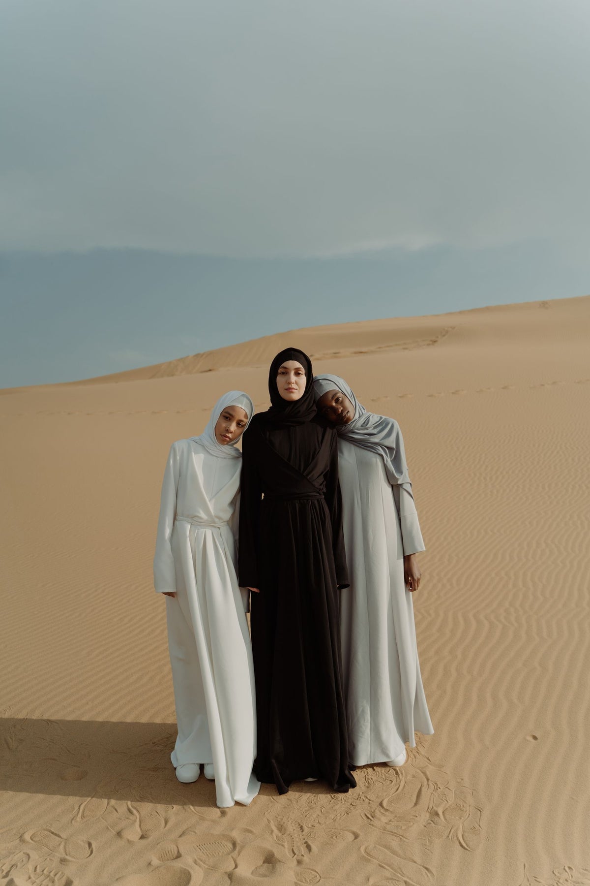 Three women in long dresses and headscarves standing together in the desert sun