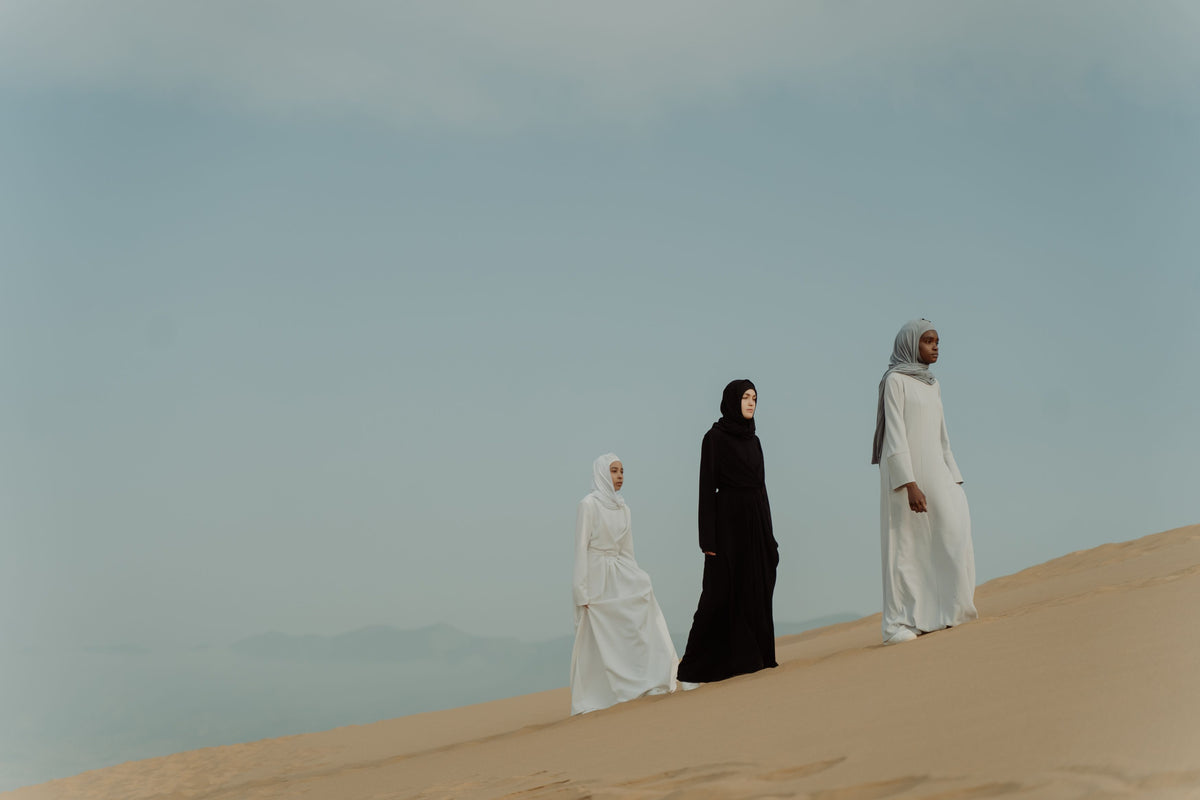 Three women walking on a desert dune under a calm sky