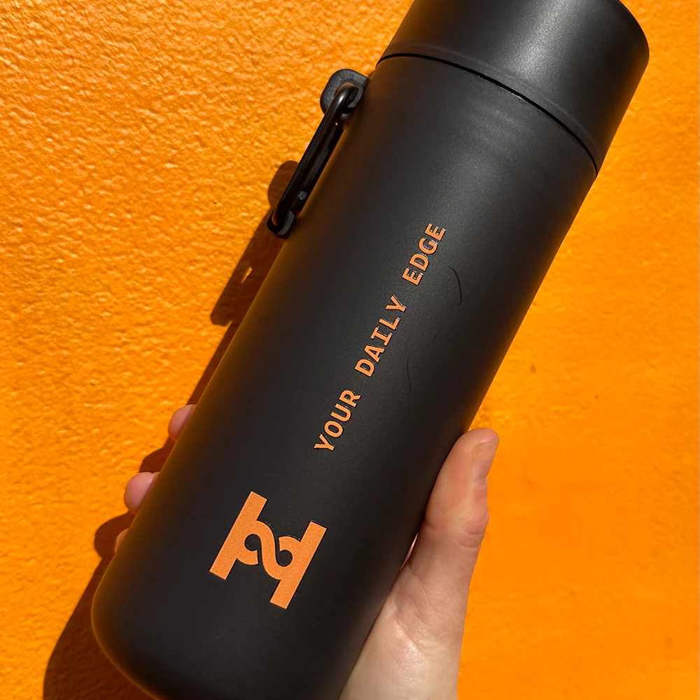 HIRO Reusable Bottle in matte black held up against an orange wall