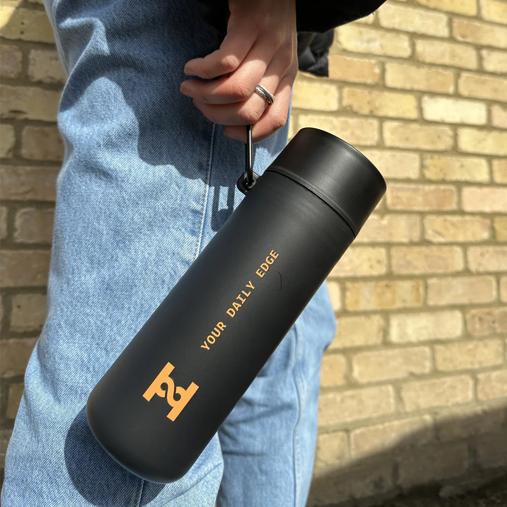 HIRO Reusable Bottle carried by its strap, matte black with orange logo