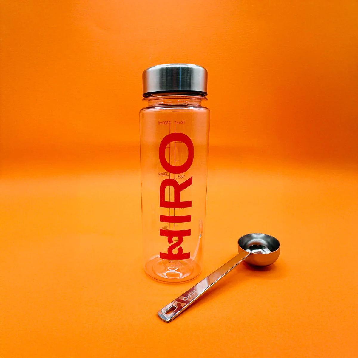 HIRO Shaker & Scoop: clear shaker bottle and metal scoop on an orange background