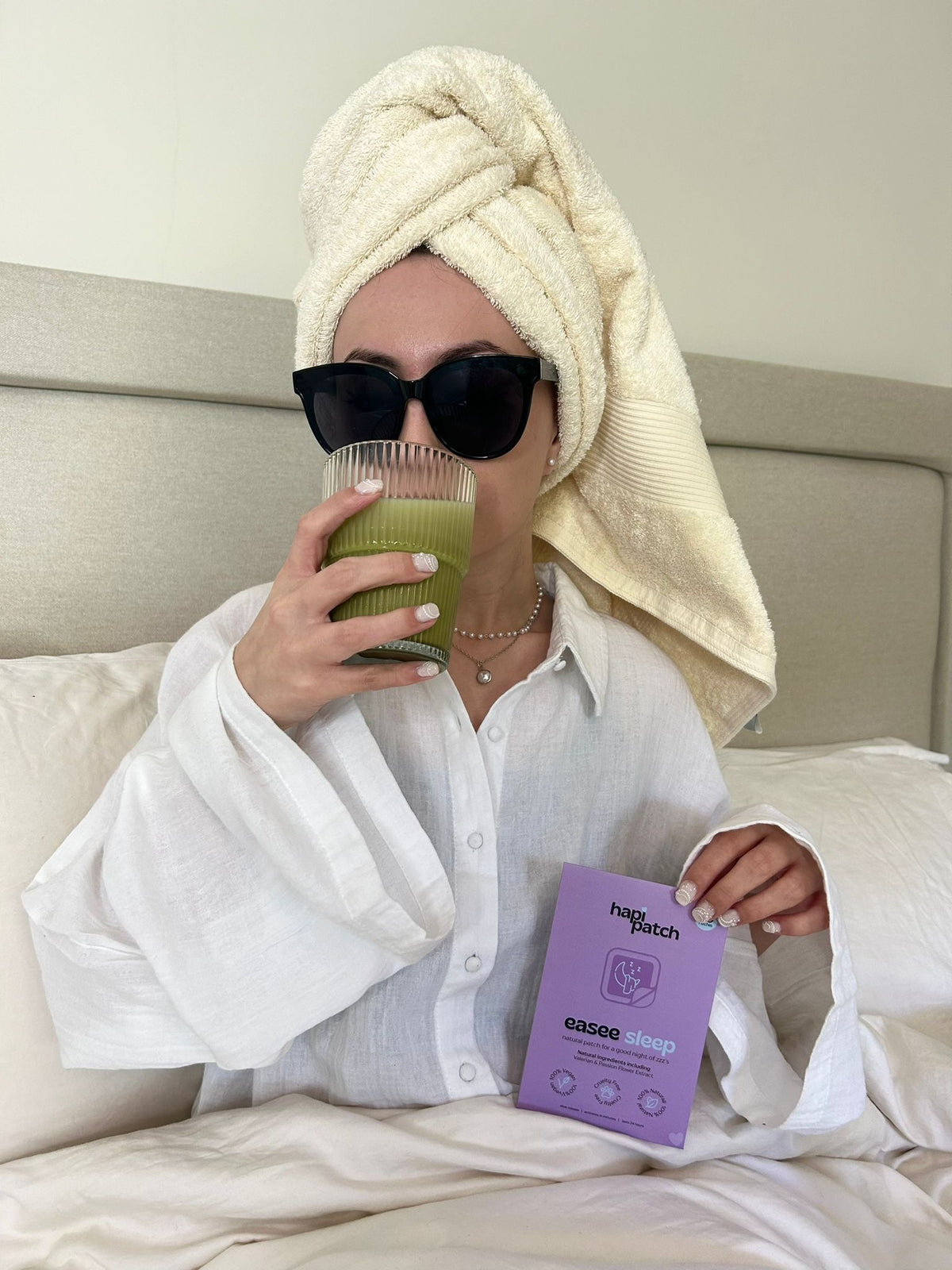 Hapi Patch Easee Sleep Patches: امرأة بمنشفة ونظارة شمسية تحمل العبوة ومشروبًا