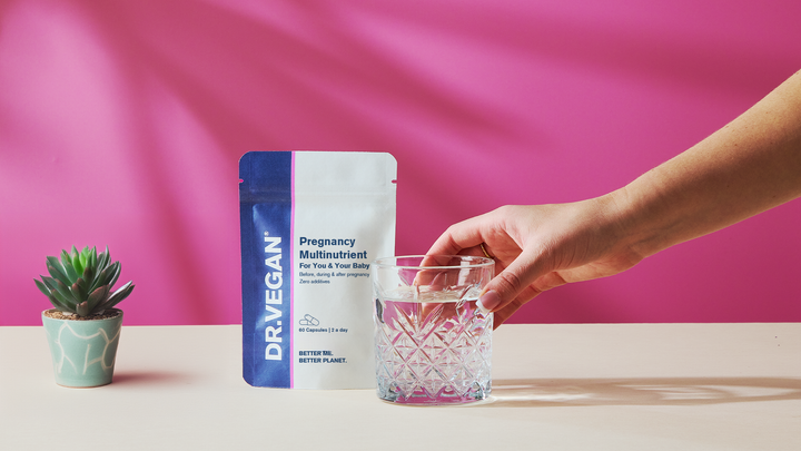 Hand reaching for a glass beside a Pregnancy Multinutrient pouch