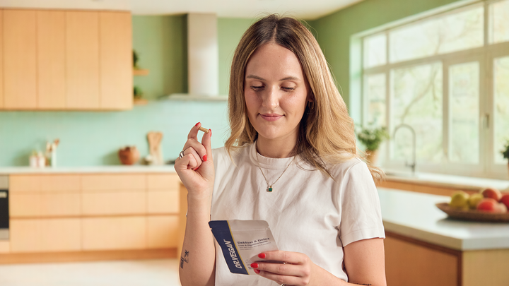 Woman in her kitchen holding a Debloat capsule