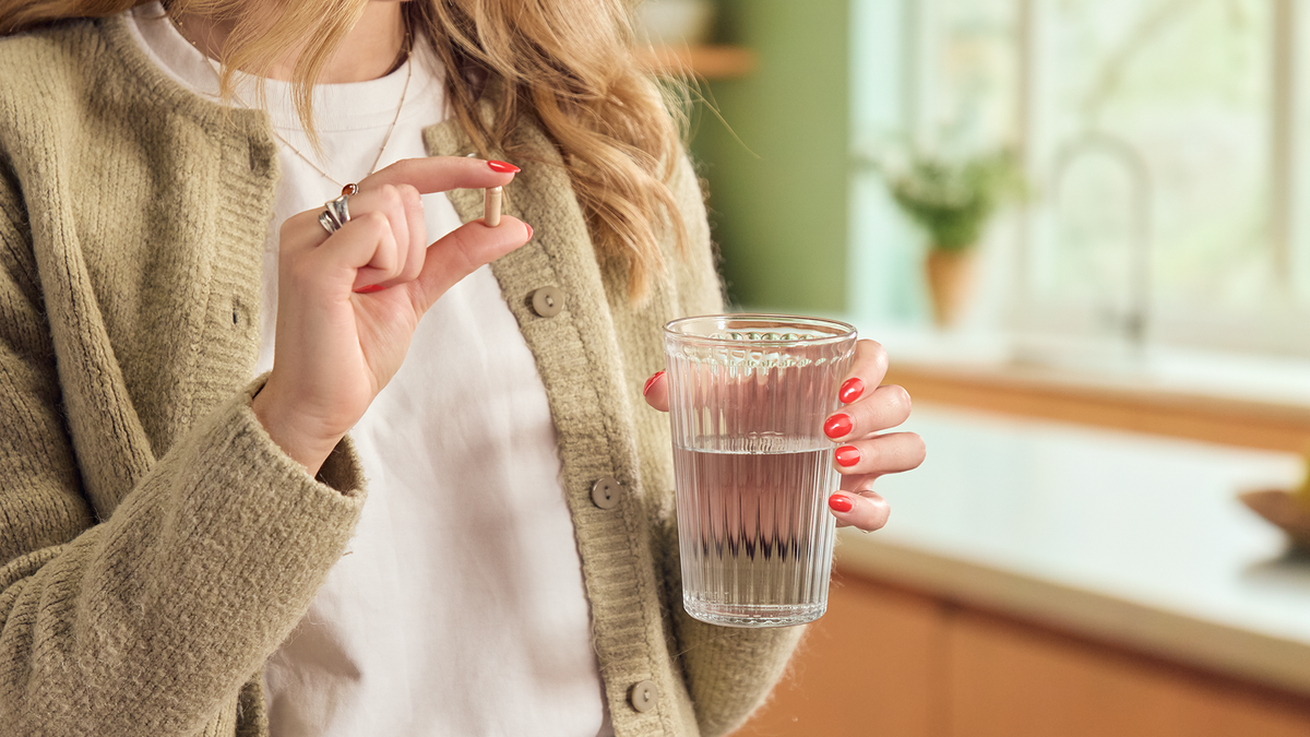 Woman taking a Skin Saviour capsule with a glass of water