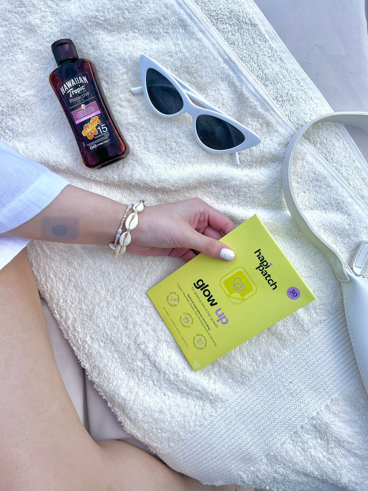 عبوة Hapi Patch Glow Up Patches على منشفة بيضاء مع نظارة شمسية وقارورة