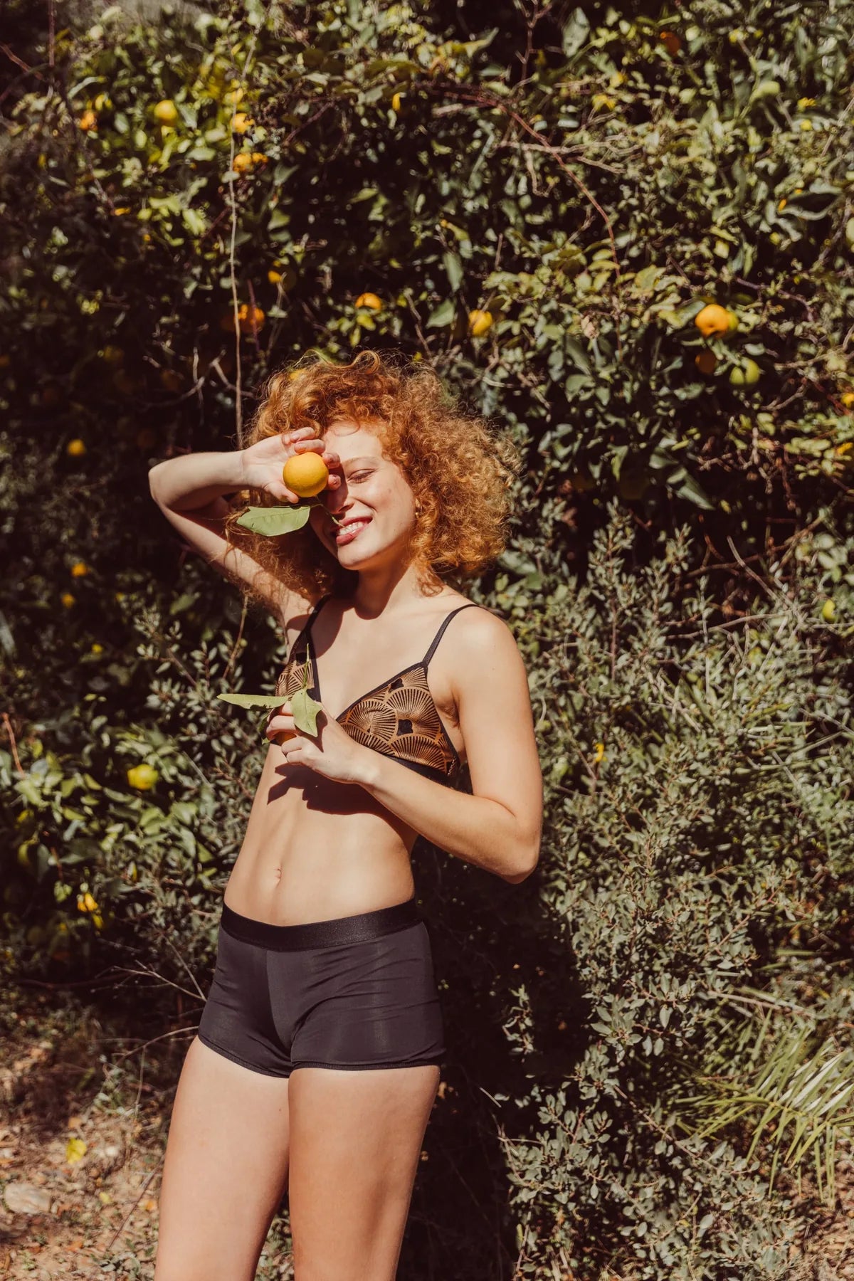 Réjeanne Glow Period Boxer in black worn by a smiling model in an orange grove